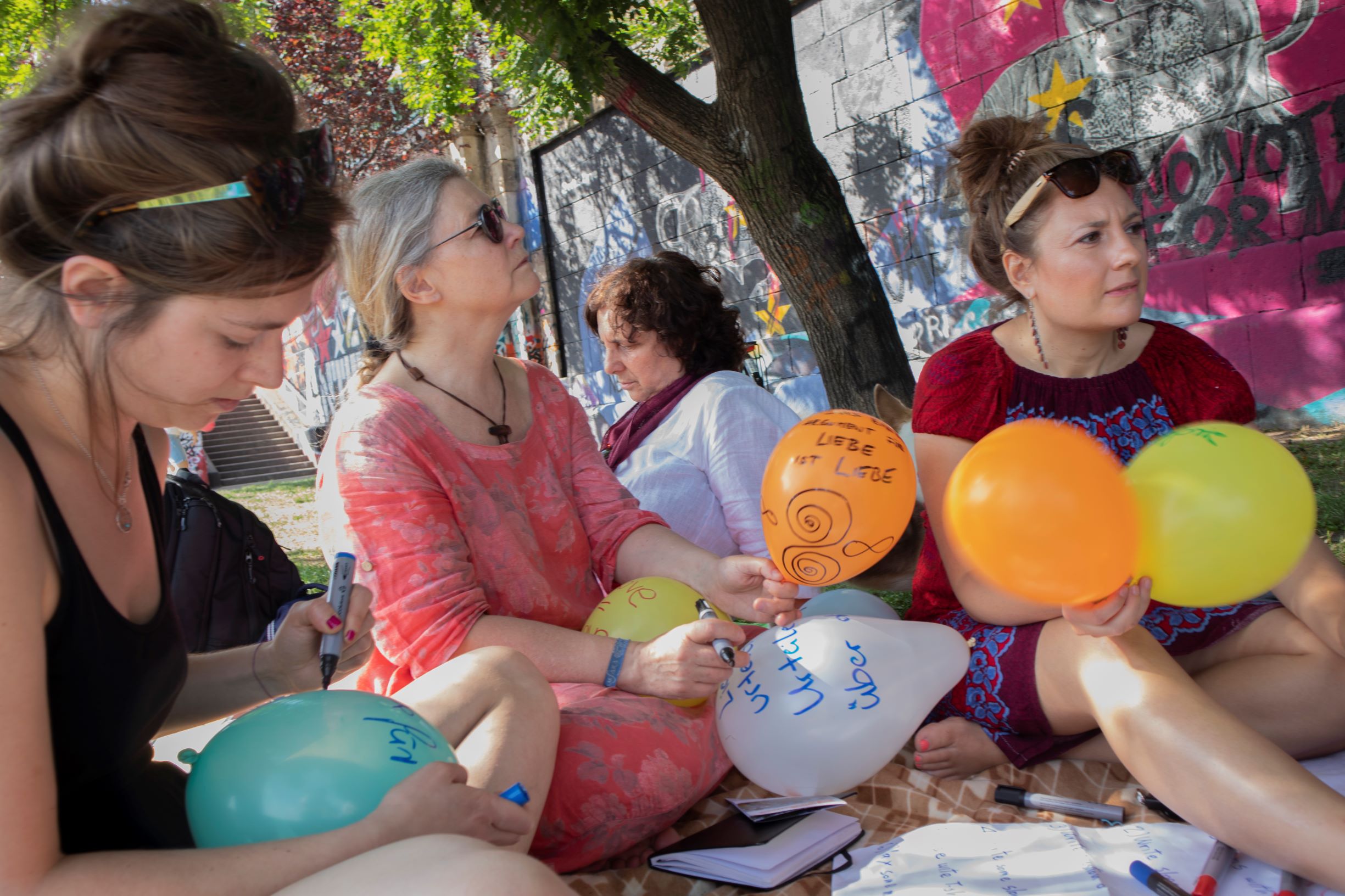 Foue woman sitting on a blanket in a park writing on the ballons